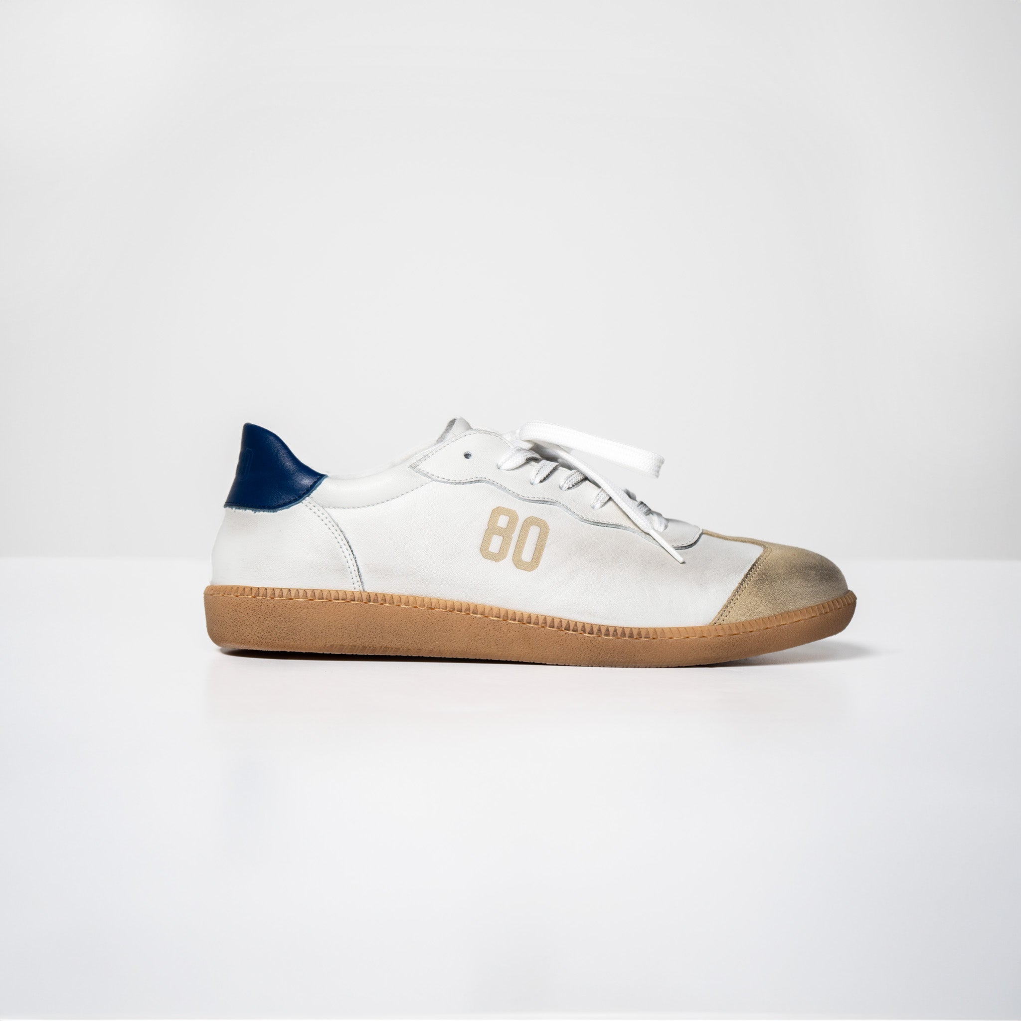 Side view of white Harvard leather sneakers with Italian rubber sole, blue heel accent, and "80" design, showcasing Italian style and craftsmanship.