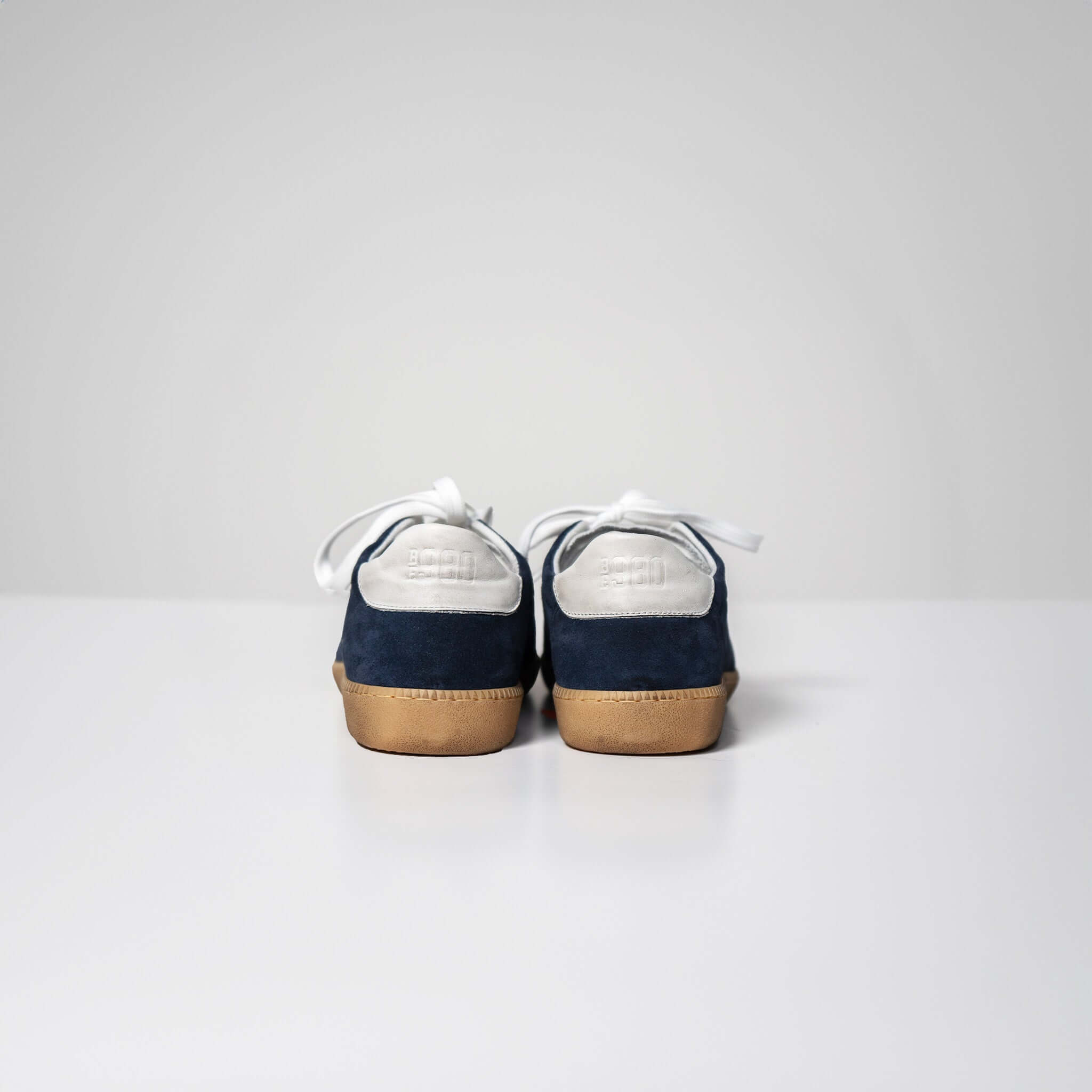 Rear view of Harvard suede sneakers in navy with Italian rubber sole and white laces on a white surface.